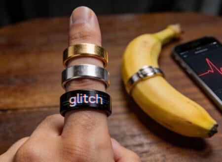 A dramatic macro shot of a human hand wearing three smart rings, with one ring physically "glitching" or sparking, and a banana in the background with a ring on it.